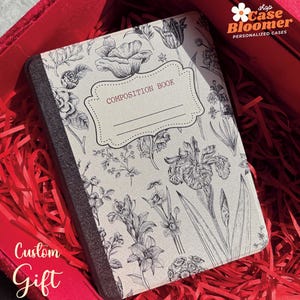 May include: A small composition book with a black and white floral design. The book is in a red gift box with red shredded paper.