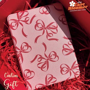 May include: A pink phone case with a red bow pattern. The case is in a red gift box with red shredded paper. The text "Custom Gift" is visible in the lower left corner of the image. The text "shop Case Bloomer PERSONALIZED CASES" is visible in the upper right corner of the image.