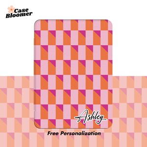 Puede incluir: Una funda de tel&eacute;fono a cuadros rosa y naranja con el nombre "Ashley" escrito en cursiva. El texto "Personalizaci&oacute;n gratuita" est&aacute; debajo del nombre.