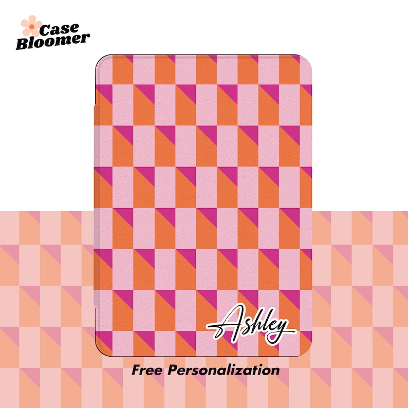 Puede incluir: Una funda de tel&eacute;fono a cuadros rosa y naranja con el nombre "Ashley" escrito en cursiva. El texto "Personalizaci&oacute;n gratuita" est&aacute; debajo del nombre.
