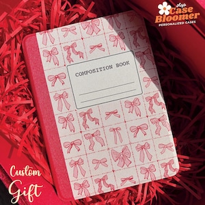 May include: A red composition book with a white cover featuring a repeating pattern of pink bows. The cover also has the text "COMPOSITION BOOK" printed in black.