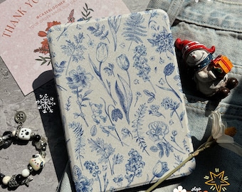 May include: A white and blue floral patterned case for an e-reader. The case has a subtle linen texture and features a variety of blue flowers and leaves.