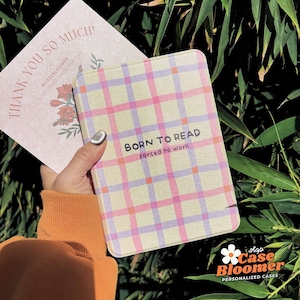 May include: A rectangular case with a pink, purple, and yellow plaid design. The text "BORN TO READ forced to work" is printed on the front. A card with the text "THANK YOU SO MUCH!" is visible in the background.