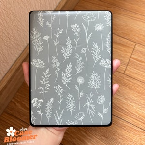 May include: A rectangular case with a gray background and a white floral pattern. The case has a black border and is held in a hand. The text "shop Case Bloomer PERSONALIZED CASES" is visible in the lower left corner.