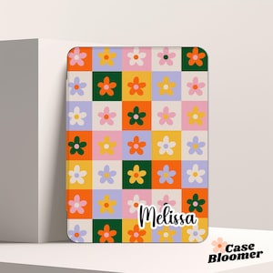 Puede incluir: Una funda de tel&eacute;fono personalizada con un patr&oacute;n de cuadros coloridos con flores en tonos naranja, amarillo, rosa y verde. El nombre "Melissa" est&aacute; impreso en negro en la funda.
