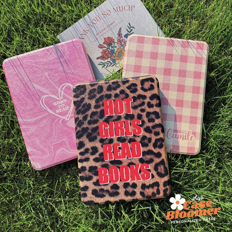 May include: Several personalised cases are displayed, each with a unique design. One case has a leopard print with the text "HOT GIRLS READ BOOKS" in red. Other cases feature pink marble, a pink gingham pattern, and a floral design with the text "THANK YOU SO MUCH!"