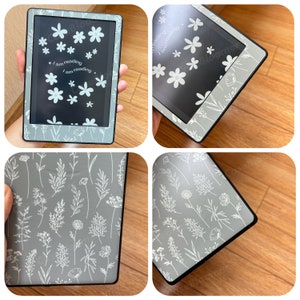 May include: A gray e-reader with a floral design. The screen displays white flowers and the text "I am reading." The e-reader has a gray border with white floral patterns. The overall design is a combination of modern and botanical elements.
