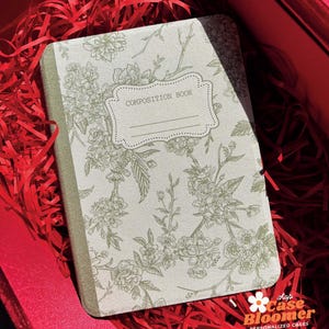 May include: A green composition book with a floral design and the text "COMPOSITION BOOK" on the front cover.