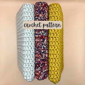 May include: Three crocheted squares stacked on top of each other. The top square is yellow, the middle square is red, white, and blue, and the bottom square is gray. The squares are all crocheted in a simple stitch. The text "crochet pattern" is written on a brown label.