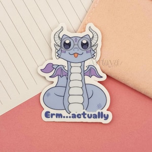 May include: A sticker featuring a cartoon dragon with a light blue body, purple wings, and the text "Erm...actually". The dragon has large eyes and a small tongue sticking out. The sticker is on a pink surface.