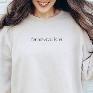 Op de afbeelding: Crèmekleurige sweatshirt met de tekst "for however long" in het zwart. De sweatshirt heeft een ronde hals en lange mouwen. De afbeelding toont de bovenste helft van een persoon die de sweatshirt draagt.