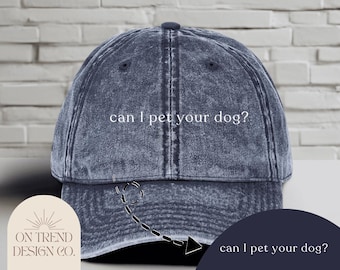 Może przedstawiać: Dżinsowa niebieska czapka bejsbolowa z białym napisem "can I pet your dog?". Czapka ma zakrzywiony daszek i guzik na górze. Czapka ma styl vintage i postarzany wygląd.