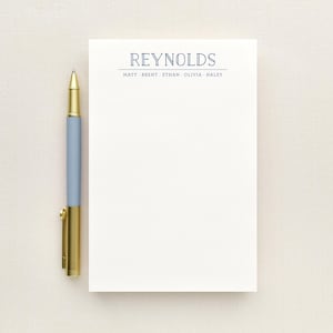 May include: A white rectangular notepad featuring the name REYNOLDS in blue text at the top, followed by the names MATT, BRENT, ETHAN, OLIVIA, and HALEY. A light blue pen with a gold clip and tip is positioned vertically along the left side of the notepad.