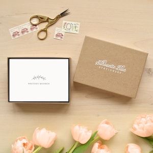May include: A box of blank stationery cards with a simple floral design and the text "Whitney Monroe" printed on the front. The box is open and the cards are visible. The box is made of brown cardboard and has the text "Silhouette Blue Stationery" printed on the front.