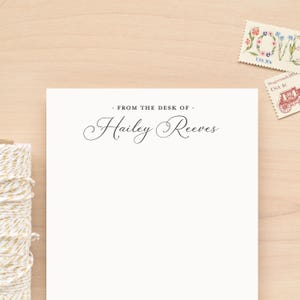 May include: Cream-colored stationery with the text "From the desk of Hailey Reeves" in elegant script. Two vintage postage stamps with floral and historical designs are in the background. A spool of twine is visible on the left.