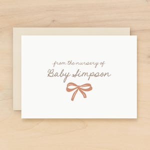 May include: A cream-colored card with a matching envelope. The card features the text "from the nursery of Baby Simpson" in a delicate script, with a bow illustration in a muted rose color.