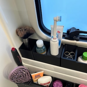 May include: A set of black plastic organizers with various toiletries and beauty products, including a toothbrush, toothpaste, a hair brush, a makeup brush, and a bottle of sunscreen.