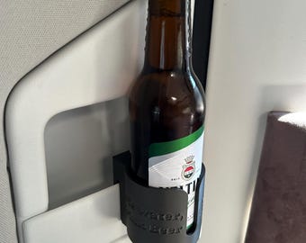 Op de afbeelding: Een zwarte plastic drinkhouder met de tekst "For Water, Not Beer" bevestigd aan een wit oppervlak. Een bruine glazen fles bier zit in de houder.