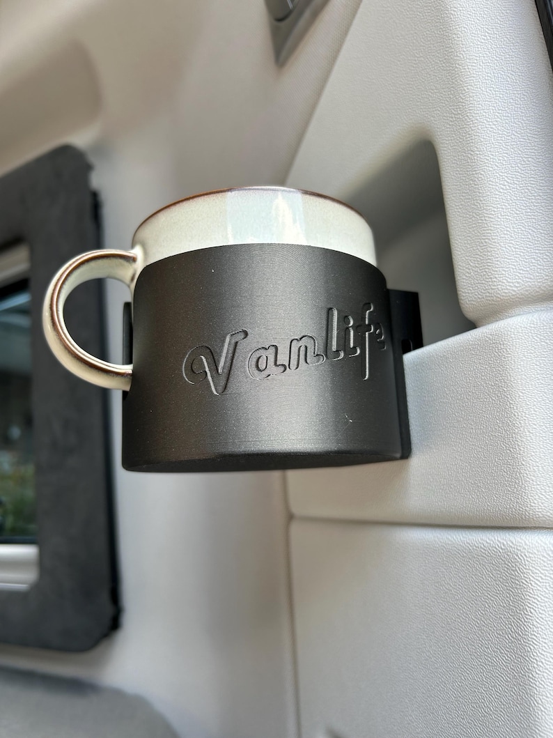 May include: A black cup holder with the word "Vanlife" embossed on it. A white ceramic mug is in the holder.