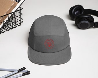 May include: A gray five-panel cap with a flat brim. The cap features a red circular logo with the text "Mad Mad Media". The cap is made of a durable fabric and is suitable for outdoor activities.