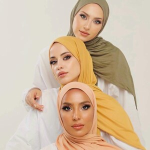 May include: Three women wearing headscarves in different colors: a light green, a yellow, and a peach. The women are looking at the camera.