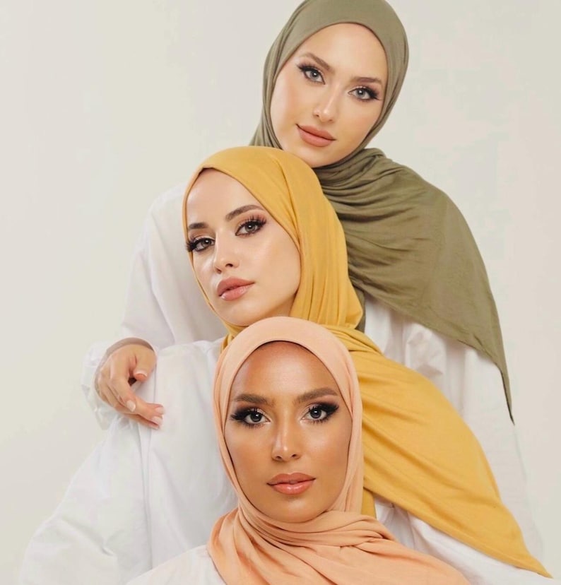 May include: Three women wearing headscarves in different colors: a light green, a yellow, and a peach. The women are looking at the camera.