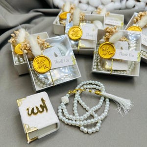 May include: White gift boxes with gold wax seals and pearl prayer beads. Each box contains a small white book with gold lettering that says "Allah". The boxes have a "Thank You" label and are decorated with dried flowers.