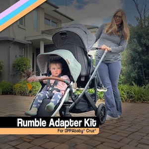 May include: A gray UPPAbaby Cruz stroller with a Rumble Adapter Kit. The stroller has a canopy and a child seated in the front. The text "Rumble Adapter Kit For UPPAbaby Cruz" is displayed at the bottom of the image.