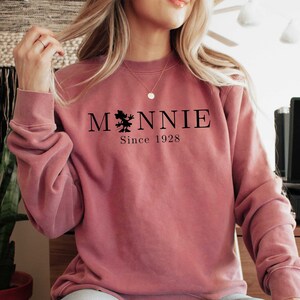 K&ouml;nnte beinhalten: Ein staubiges rosafarbenes Sweatshirt mit einer schwarzen Grafik eines Baumes und dem Text "MONNIE Since 1928"
