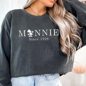 K&ouml;nnte beinhalten: Ein dunkelgrauer Pullover mit einem wei&szlig;en Aufdruck von Mickey Mouse und dem Text "M*NNIE Since 1928".