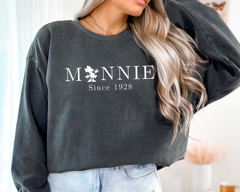 K&ouml;nnte beinhalten: Ein dunkelgrauer Pullover mit einem wei&szlig;en Aufdruck von Mickey Mouse und dem Text "M*NNIE Since 1928".