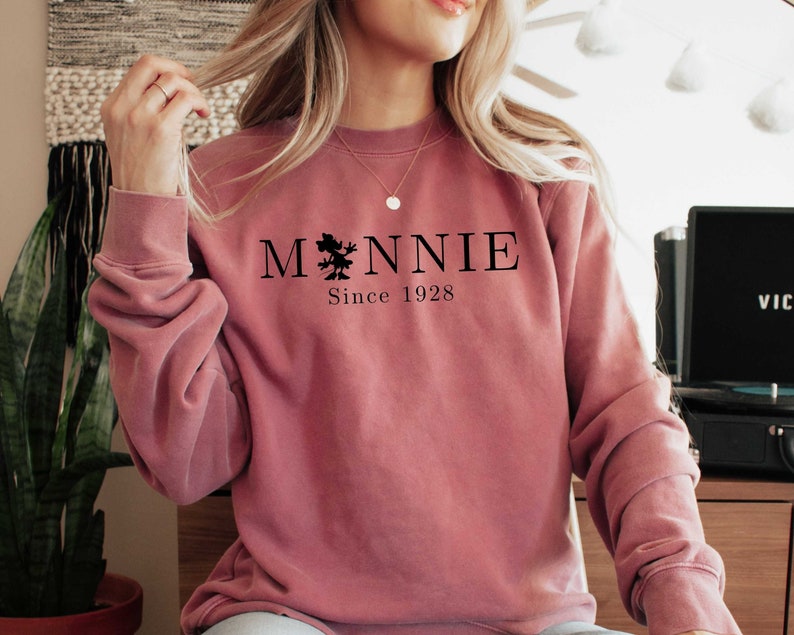 K&ouml;nnte beinhalten: Ein staubiges rosafarbenes Sweatshirt mit einer schwarzen Grafik eines Baumes und dem Text "MONNIE Since 1928"