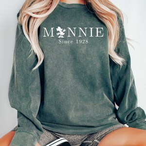 K&ouml;nnte beinhalten: Ein dunkelgr&uuml;ner Pullover mit einer wei&szlig;en Grafik, auf der "MONNIE Since 1928" steht.