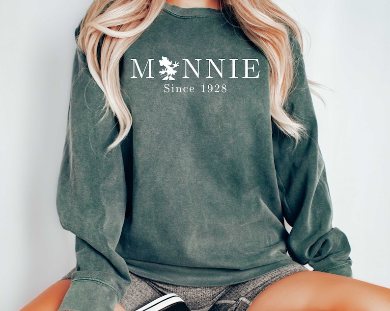 K&ouml;nnte beinhalten: Ein dunkelgr&uuml;ner Pullover mit einer wei&szlig;en Grafik, auf der "MONNIE Since 1928" steht.