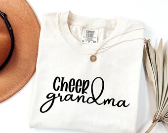 May include: A white t-shirt with the text "Cheer grandma" in black cursive lettering.