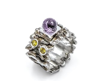 May include: A silver ring with a textured, organic design. The ring features a large purple gemstone and two smaller yellow gemstones.