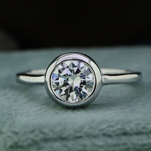 May include: A silver ring with a bezel setting featuring a round, clear diamond.