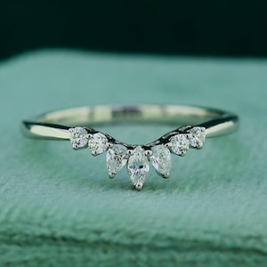 May include: A delicate silver ring with a curved design. The ring features a series of small, round, and marquise-cut clear gemstones. The gemstones are set in a symmetrical pattern, creating a sparkling and elegant look. The ring is set against a soft green background.