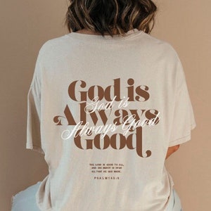Könnte beinhalten: Beiges T-Shirt mit dem Text "God is Always Good" in braunen Buchstaben. Das Shirt zeigt auch den Text "The Lord is good to all, and his mercy is over all that he has made. Psalm 145:9". Die Person trägt eine hellblaue Jeans.