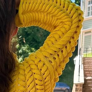 May include: A bright yellow long-sleeve sweater featuring a prominent vertical cable knit pattern with openwork detailing between the textured columns. The garment has a high neckline and a thick, chunky knit construction throughout the sleeves and body.