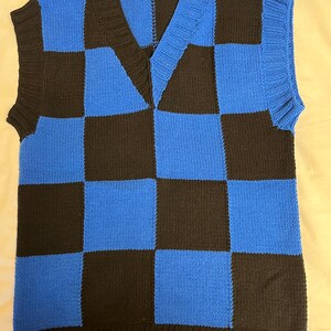 May include: A blue and black checkerboard pattern knitted vest with a V-neck. The sleeveless garment has a ribbed hem and trim. The color scheme is a bold combination of black and bright blue, creating a striking visual contrast.