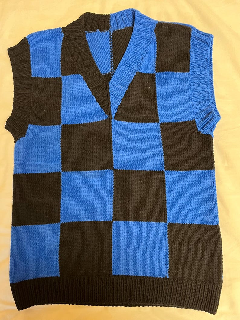 May include: A blue and black checkerboard pattern knitted vest with a V-neck. The sleeveless garment has a ribbed hem and trim. The color scheme is a bold combination of black and bright blue, creating a striking visual contrast.