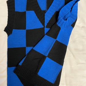 May include: A blue and black checkerboard pattern sweater vest with a matching long sleeve. The V-neck vest and sleeve are made of a knitted material. The color scheme is a bold combination of black and blue.