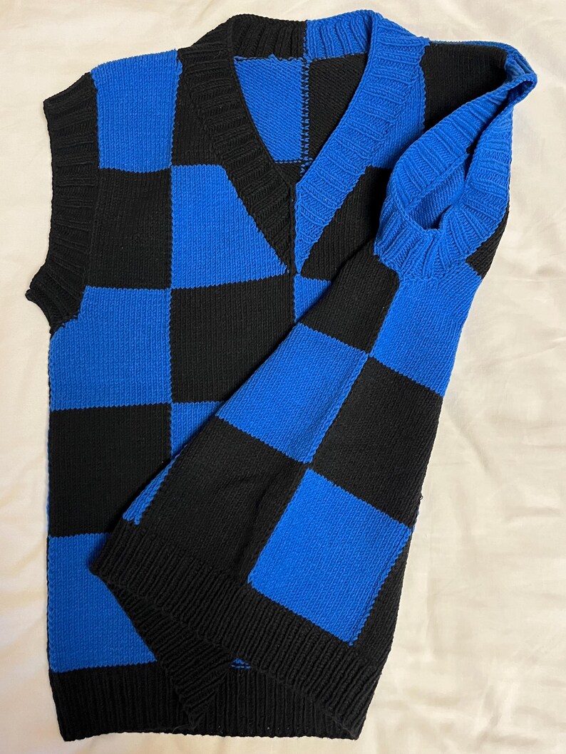 May include: A blue and black checkerboard pattern sweater vest with a matching long sleeve. The V-neck vest and sleeve are made of a knitted material. The color scheme is a bold combination of black and blue.