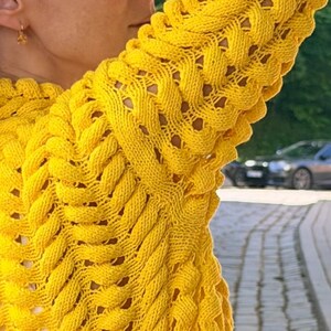 May include: A bright yellow long-sleeve sweater featuring a prominent, raised cable knit pattern that runs vertically along the sleeves and body. The knit construction creates a textured, braided appearance with small open spaces between the thick yarn.