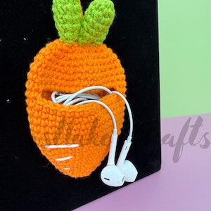 May include: A handmade orange crochet carrot-shaped pouch with green leaves at the top. White earbuds are coming out of the pouch. The pouch has white stripes and an orange string for hanging. A fun and unique accessory.