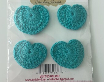 Puede incluir: Cuatro corazones de ganchillo turquesa en un paquete. El paquete lleva la etiqueta "Bella BLVD Crochet Hearts" y "GULF HEARTS". También se puede leer el texto "VISIT US ONLINE: www.bellablvd.net bellablvd.typepad.com".