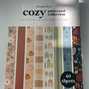 May include: A "Cozy Patterned Collection" scrapbook paper set by Scrapbook.com. The package features various patterned sheets with fall themes, including pumpkins, houses, and floral designs. The set contains 40 sheets of 230 GSM paper.