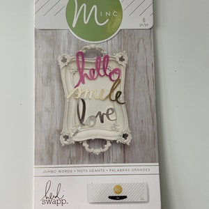 Puede incluir: Un paquete de seis palabras de lámina dorada y rosa, "hello", "smile" y "love", en un marco blanco. El paquete está etiquetado como "Jumbo Words" y "Minc" con instrucciones para usar con un aplicador de lámina y lámina.
