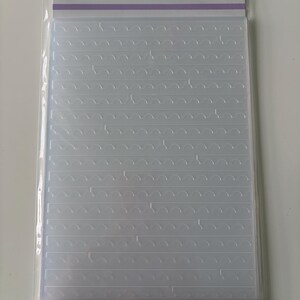 Może przedstawiać: Przezroczysta plastikowa teczka do wytłaczania ze wzorem powtarzających się fal. Teczka jest oznaczona jako "EMBOSSING folder OF THE month APRIL 2023" i "PERFORATED STAMP EDGES". Widoczna jest również nazwa marki "SPELLBINDERS clubs".